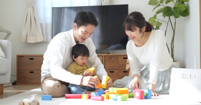 家で父親、母親、幼い子どもが遊んでいるイメージ