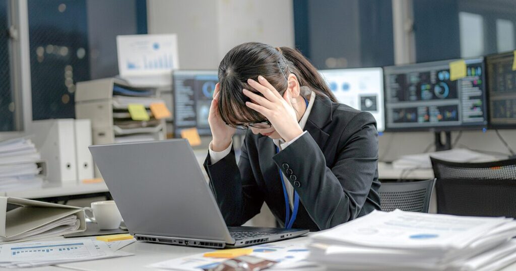 職場で悩みを抱え辞めたいと頭を抱えて悩む新卒社員のイメージ