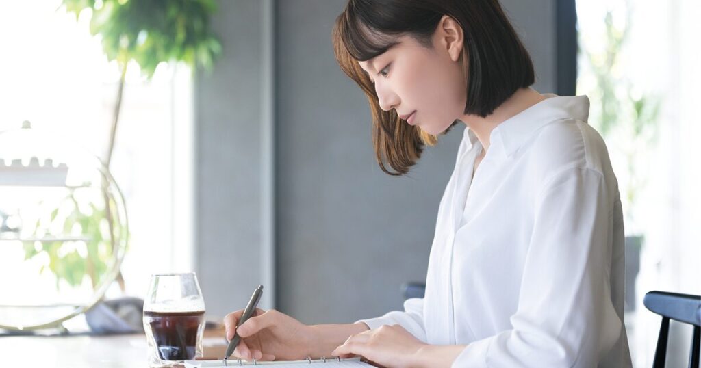 退職するべきか冷静に考えながら状況を整理してメモをとる新卒社員のイメージ
