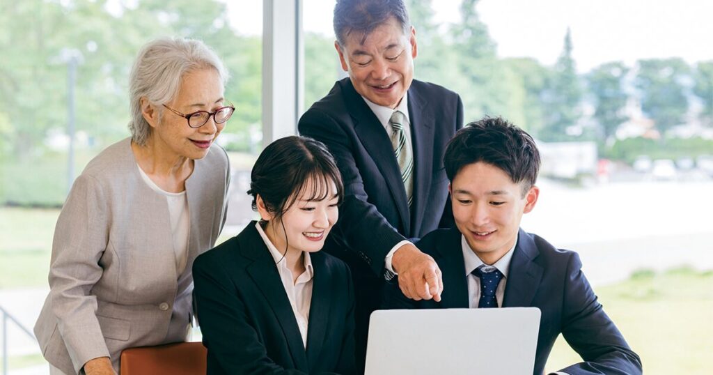 オフィスで若手社員と一緒に仕事を進める定年後のシニア世代の男女