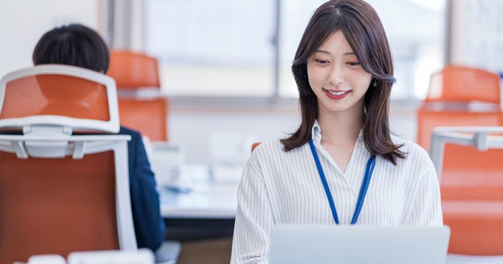 オフィスの自席でパソコンを使って仕事をしている女性